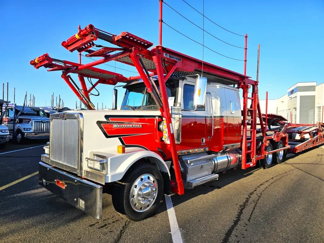 Red and white Western Star car hauler truck with empty racks parked on asphalt.
