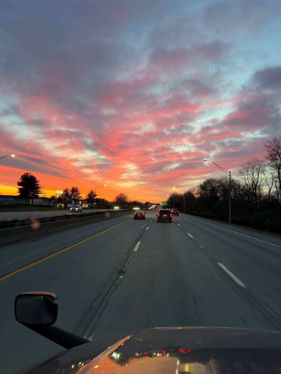 Vibrant pink and orange sunset over a multi-lane highway with cars driving towards the horizon.